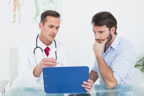 Male doctor discussing reports with patient at desk in medical o